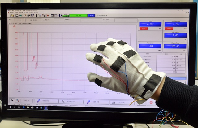 ETRI연구진이 그래핀 기반 직물형 스트레인-압력복합센서를 면장갑에 적용해 손동작에 따른 신체신호 감지 기술을 인장·압축 측정 장비를 통해 시연하고 있는 모습.<사진=ETRI 제공> 
